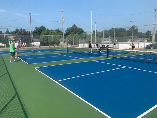 people playing pickleball on smooth well-kept courts in Sudbury under a clear blue summer sky.