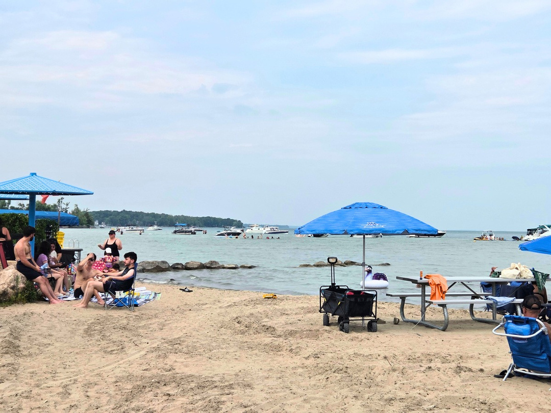 Leonard Beach, with light sugary sand dotted with sunbathers and umbrellas along a pale blue Lake Simcoe on a breezy summer day. 