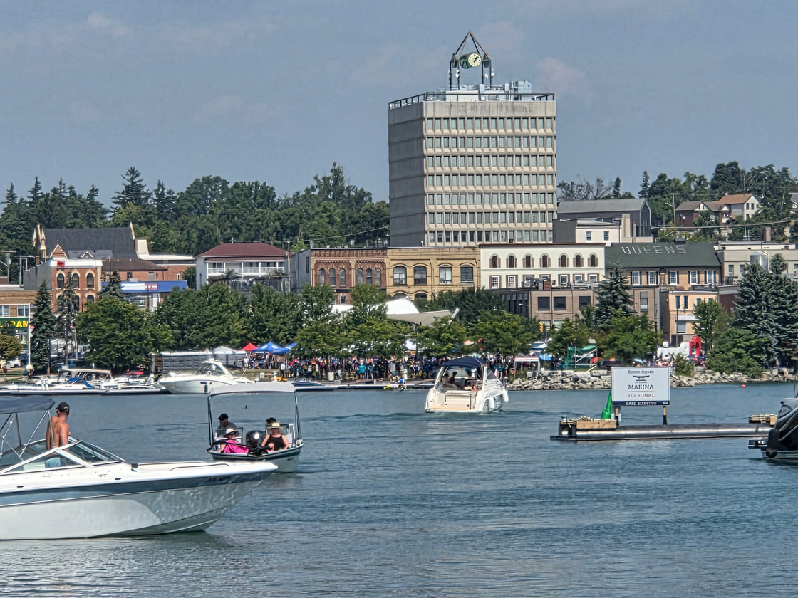 a bustling marina and beachfront filled with people enjoying the summer sun, with the city of Barrie waterfront in the background.