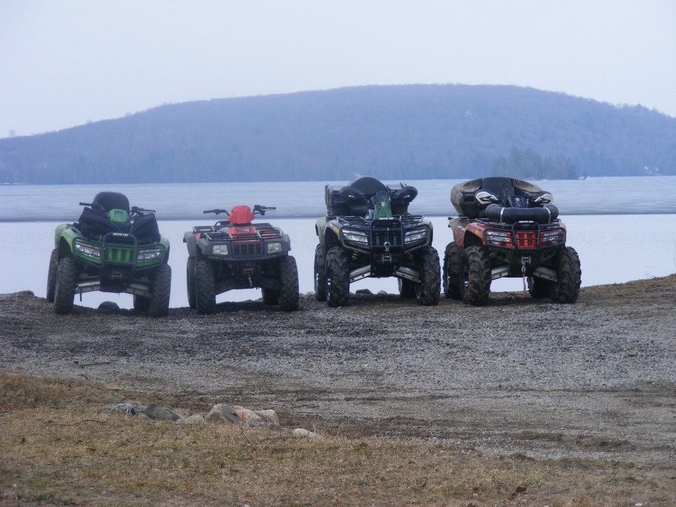 At Edgewater Park Lodge, a row of ATVs sit on the beach with a misty lake and forested island behind them.