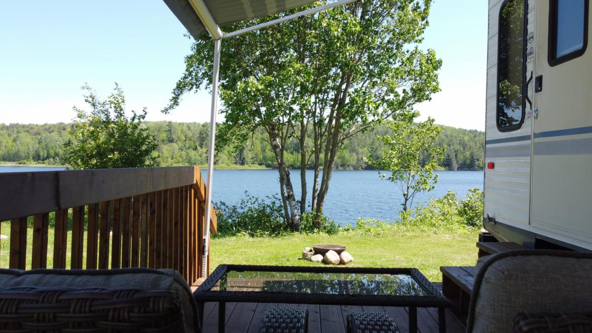 lounge chairs next to an RV facing toward a blue lake and bright green trees at on a sunny summer day at Lazy Rock Campground.