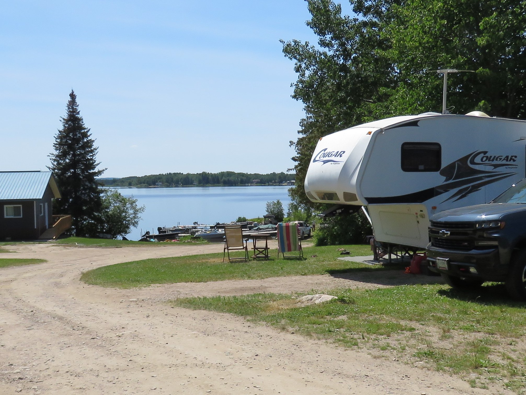 a RV sits in a grassy campsite along a gravel trail by a blue lake at Booth Landing Camping.  