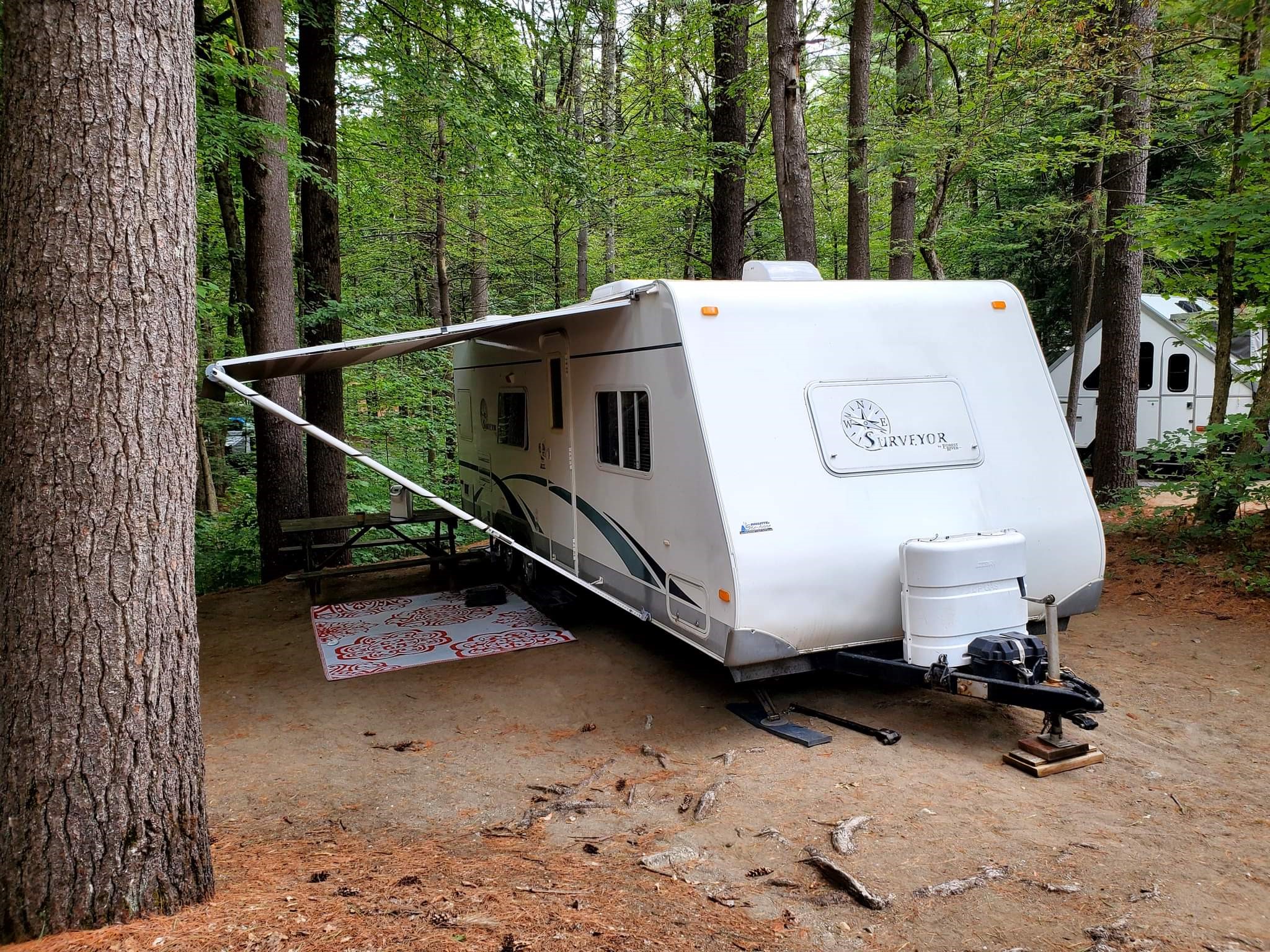 an RV set up in a tidy, packed-earth campsite shaded by thick green forest at Rock Lake Campground.