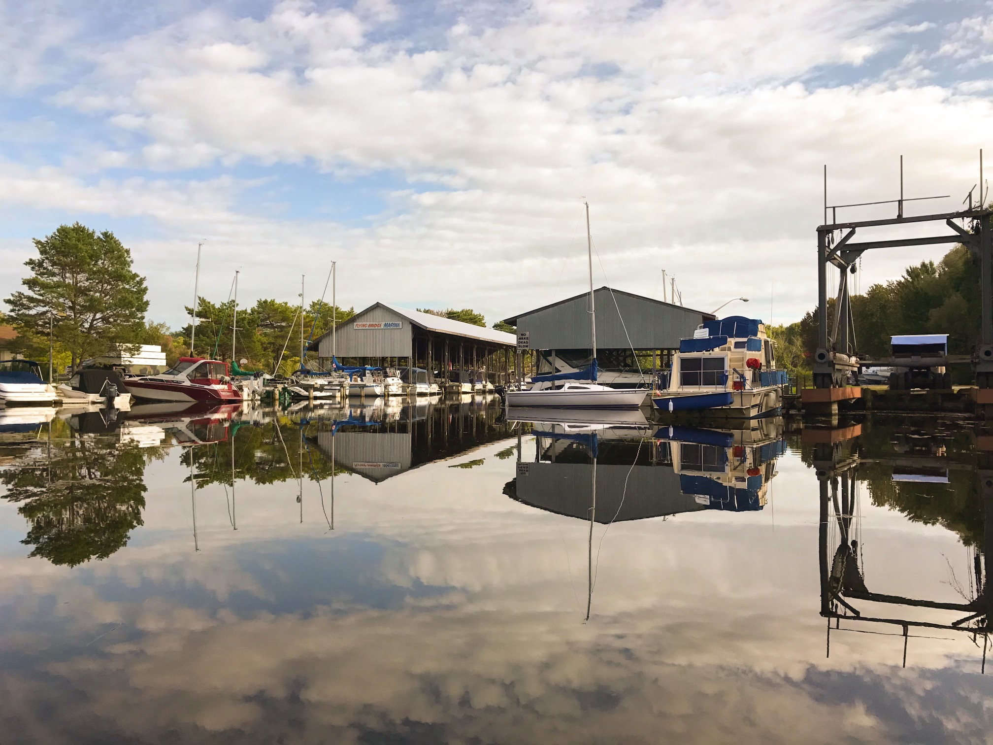 glassy water reflects the golden summer sky at sunset while boats sit peacefully in the covered slips along the shore at Flying Bridge Marina. 