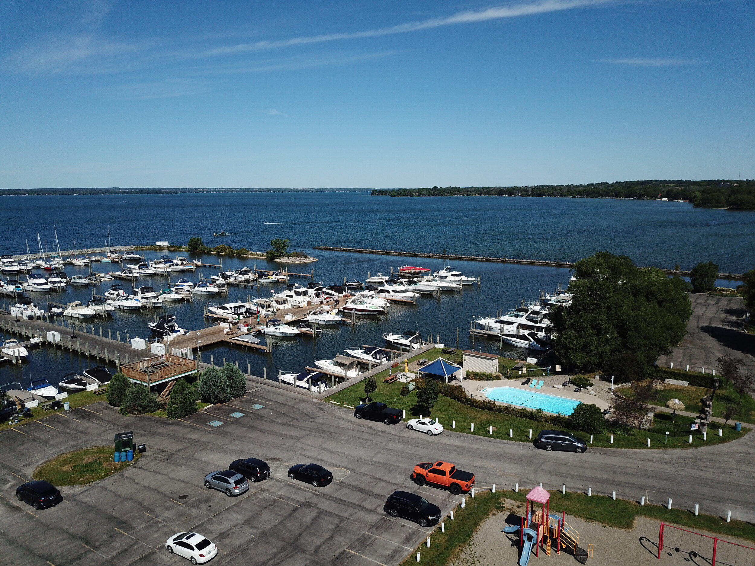 A busy Krates Marina, with cars pulling up to the water's edge while boats move in and out of the slips on a clear summer day. 