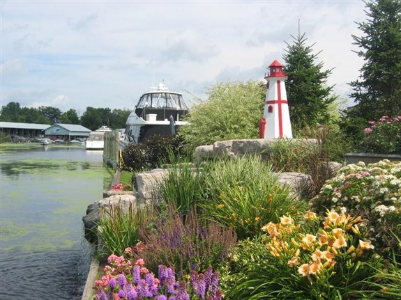 colourful flowerbeds and lush landscaping on the edge of the water at Krates Marina, decorated with a small model lighthouse. 