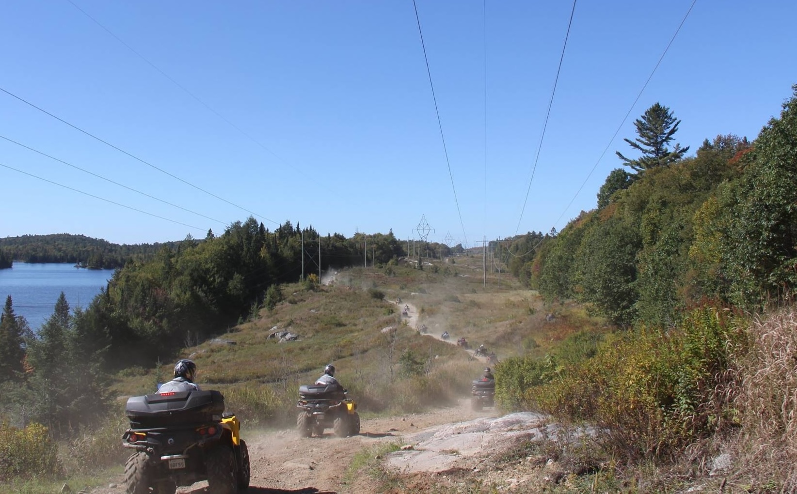 a line of ATVers ride along a gravel trail rolling over forested hills into the distance on the Voyageur Multi Use Trail. 