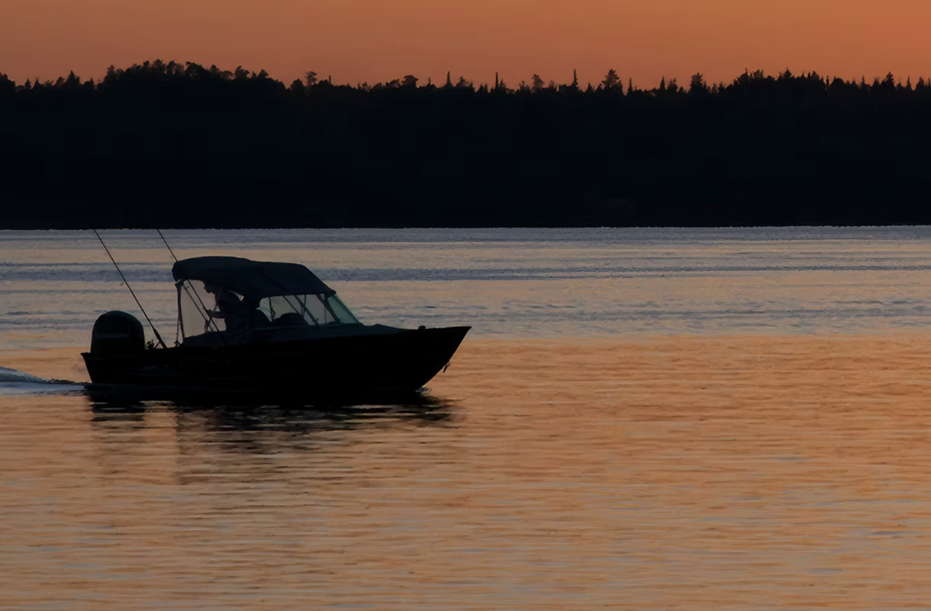 A boat sails calmly under an orange sunset at a quiet Everglades Marina. 