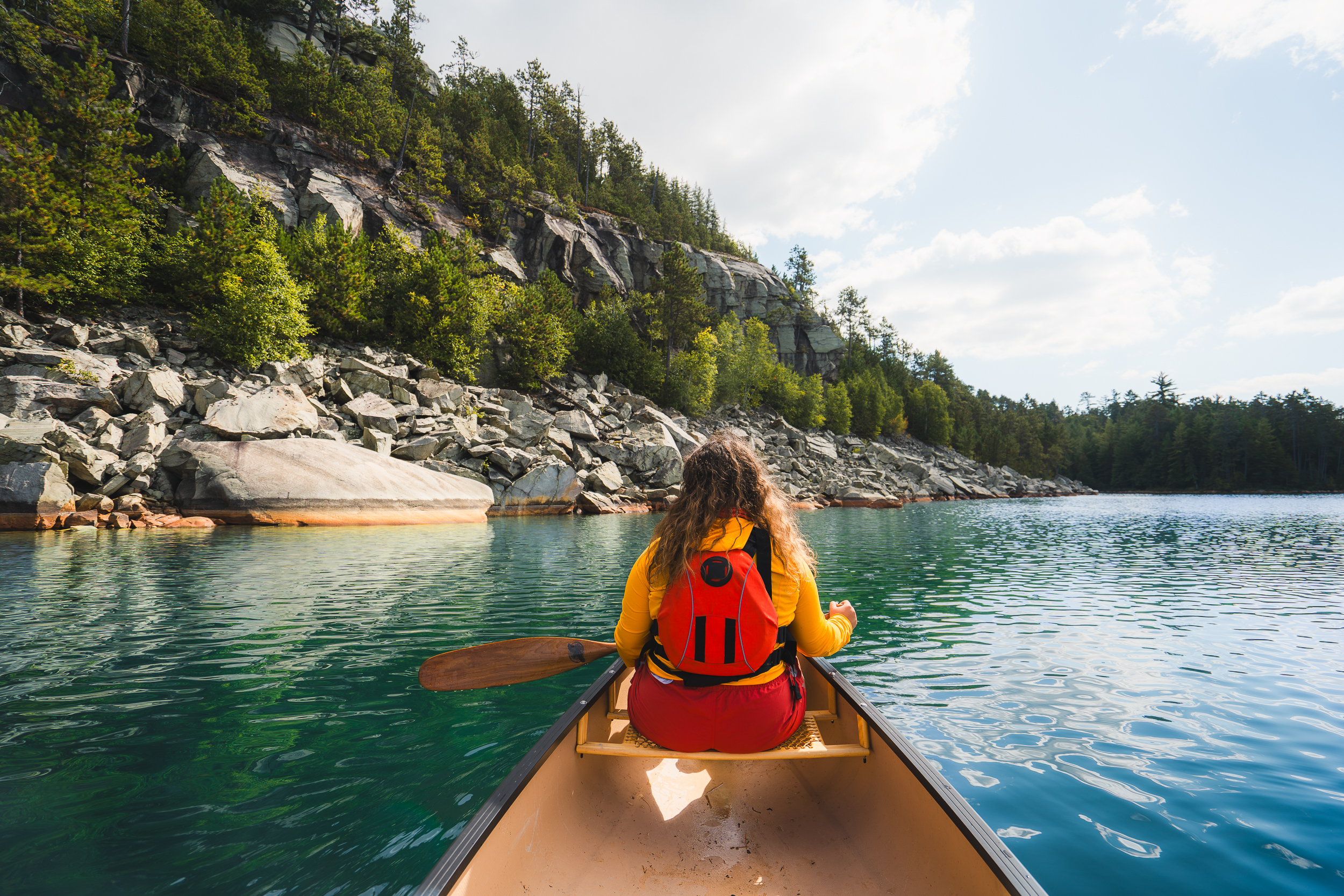 Person in bow of canoe holding a a paddle on a glassy turquoise lake with trees in background