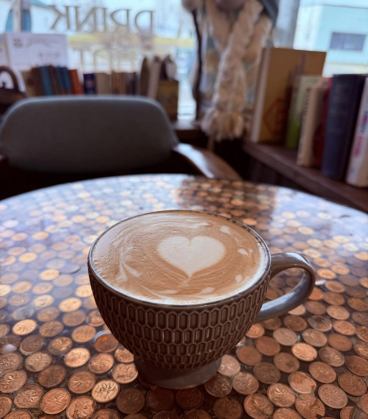 a small latte artfully decorated with a creamy foam heart on top sits on a table made of shellacked copper pennies at the Copper Bean Cafe in Bruce Mines.