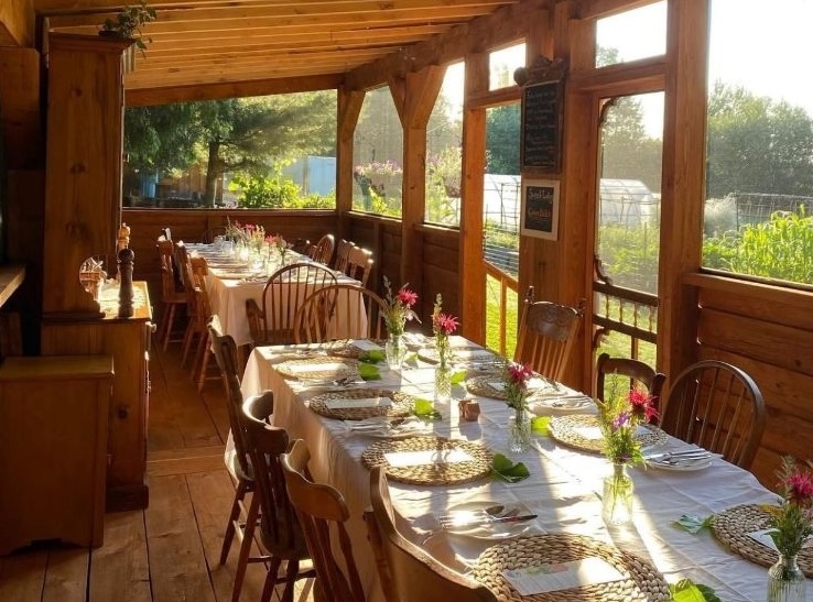 a sunny wooden patio with long tables elegantly set for dinner, overlooking a green orchard in North Bay.
