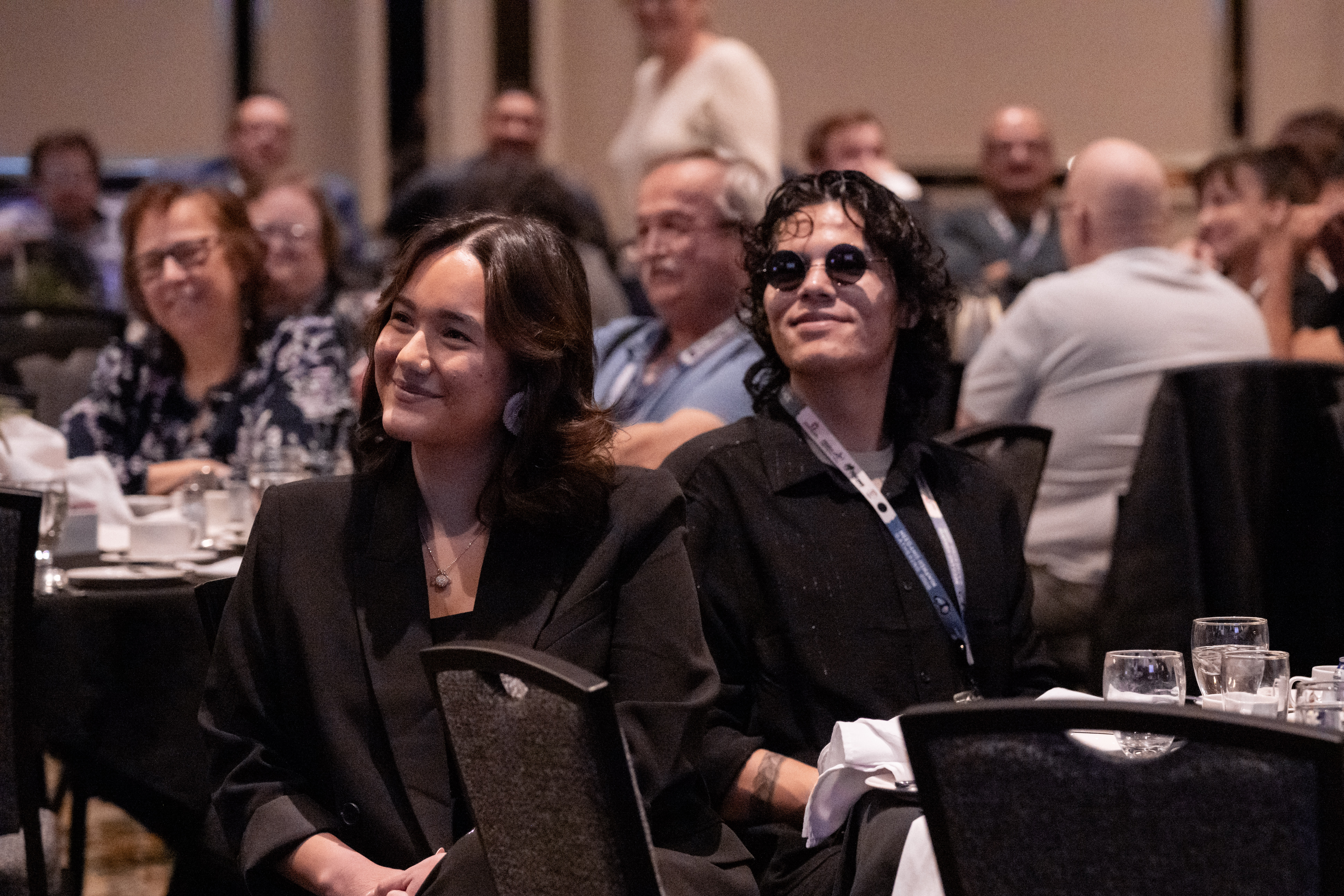 two event attendees smile warmly at their table as they listen to a presentation in Thunder Bay.