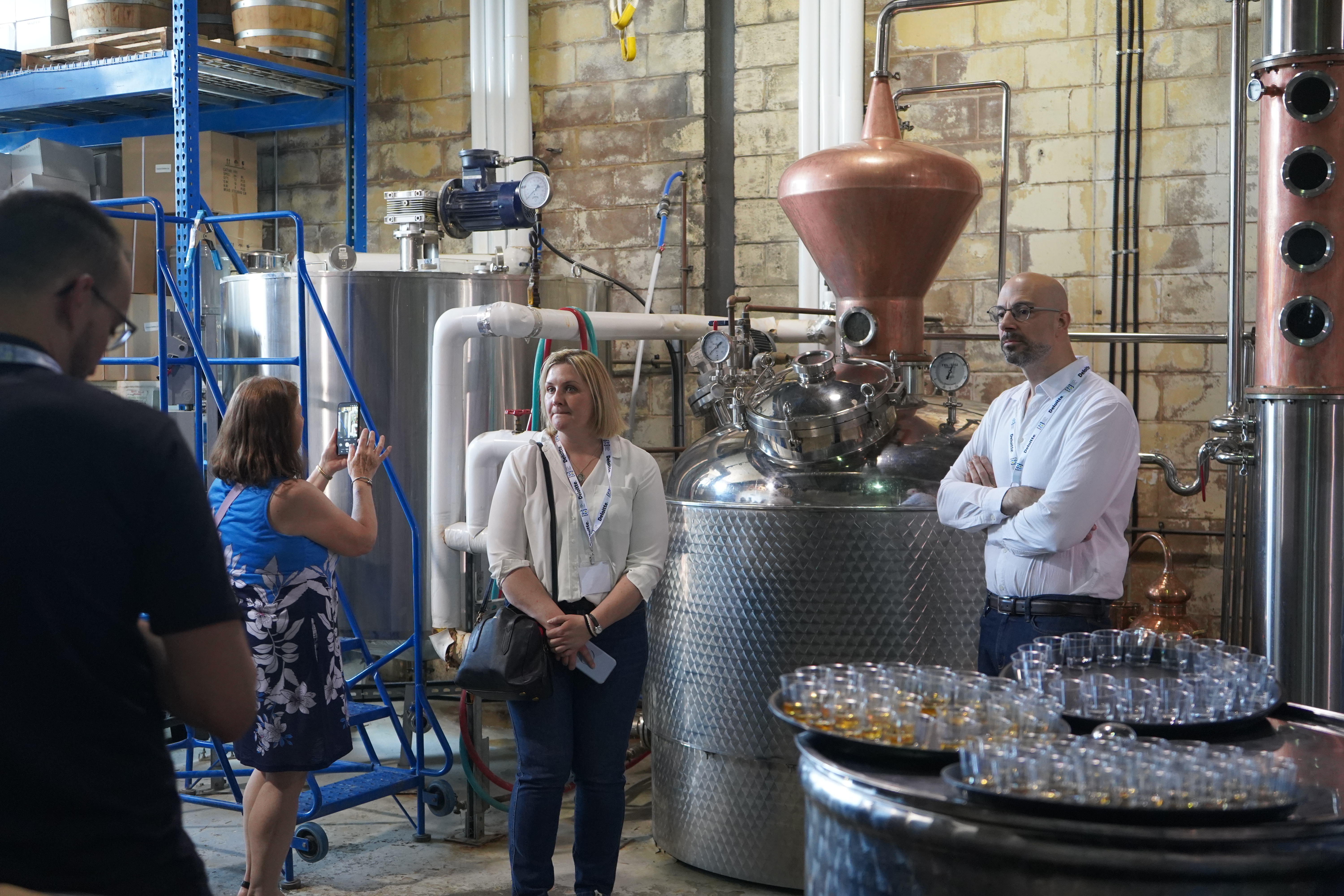 two people wearing delegate badges stand for a photo in front of the equipment at Crosscut Distillery. 