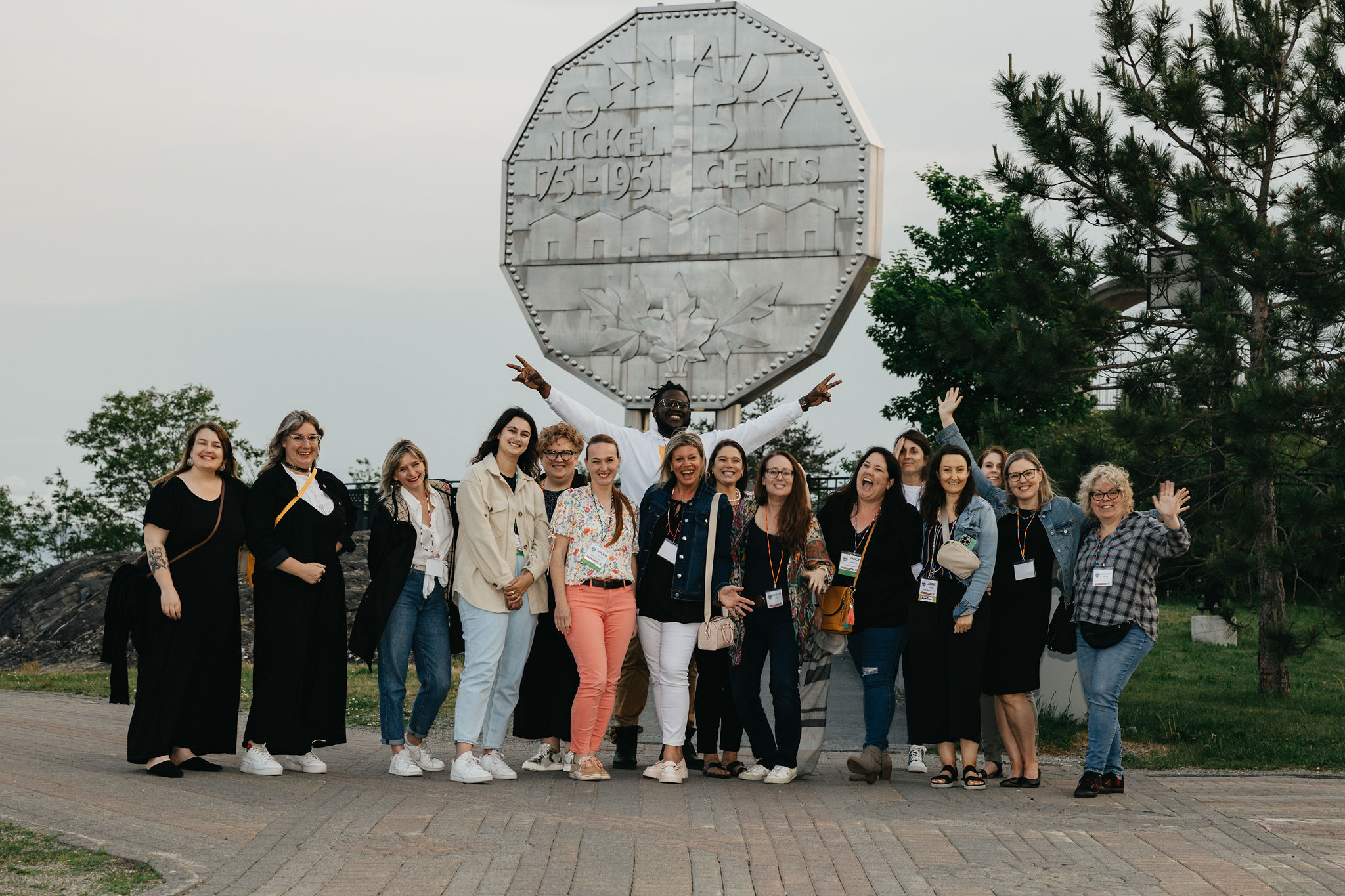 a group of smiling delegates wearing badges pose in front of the Big Nickel in Sudbury.