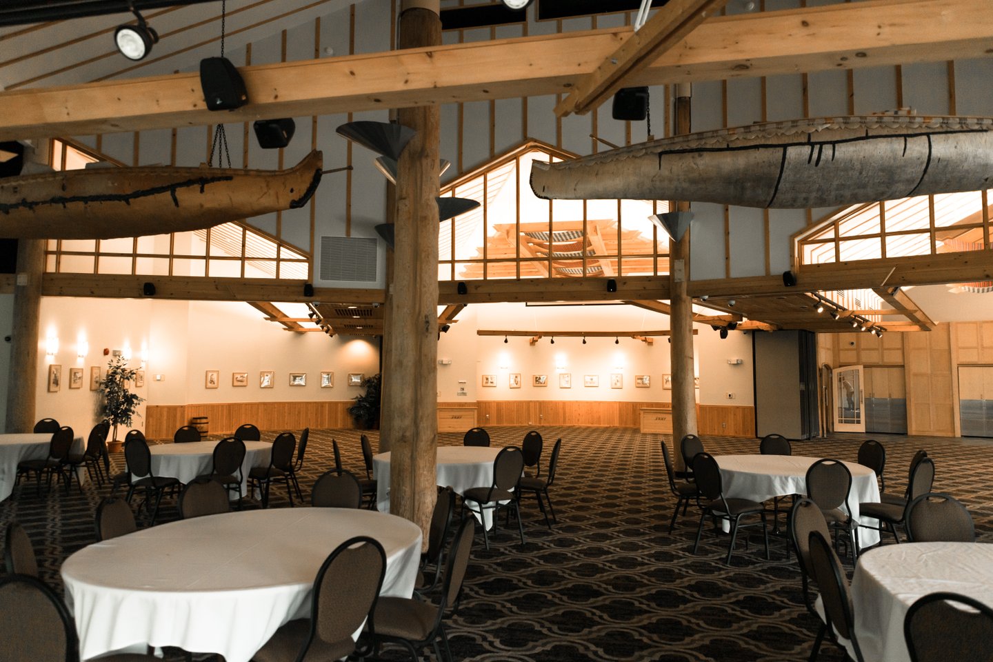 Round tables set for meeting guests under soft lighting among the wooden pillars at Fort William Historical Park McGillvray's Landing. 