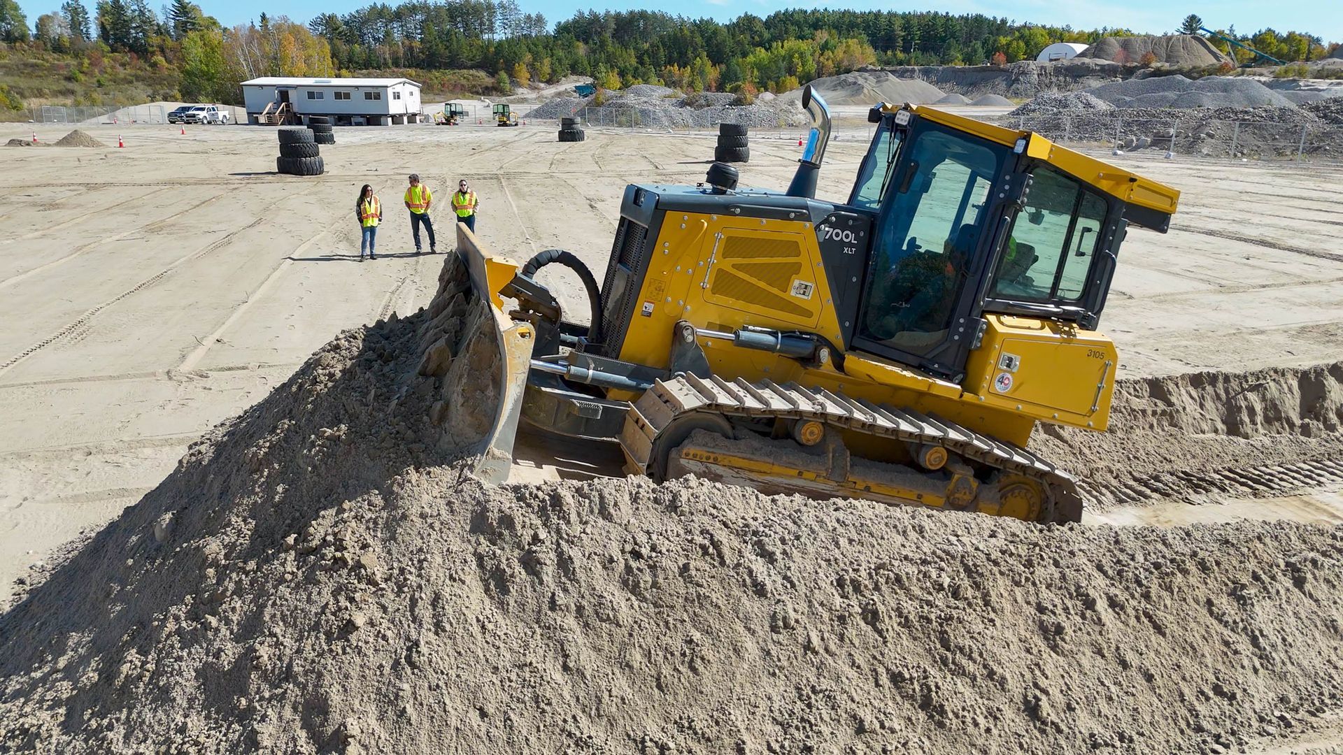 A bulldozer pushes up a large mound of soft dirt while a group of colleagues looks on from far below at MASHinery.