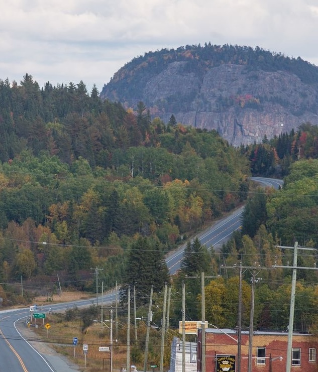 The rocky dome of Mount Cheminis stands high above a town in an autumnal forest at the end of a winding road.