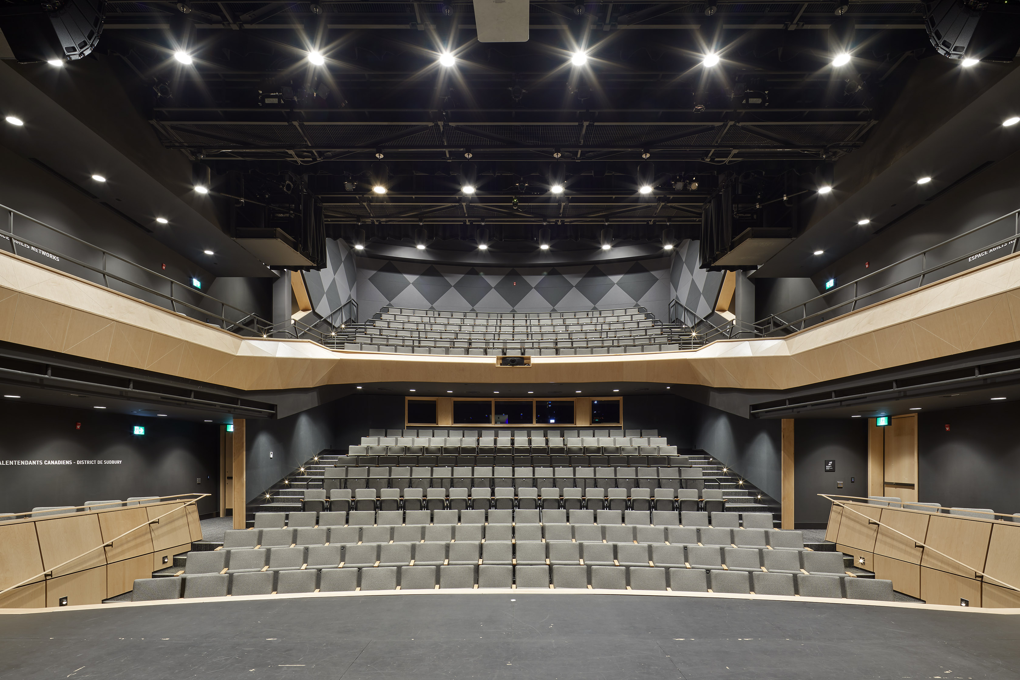 La Grande Salle at Place des Arts in Sudbury, a lit auditorium with row after row of seating inluding a balcony overhead. 