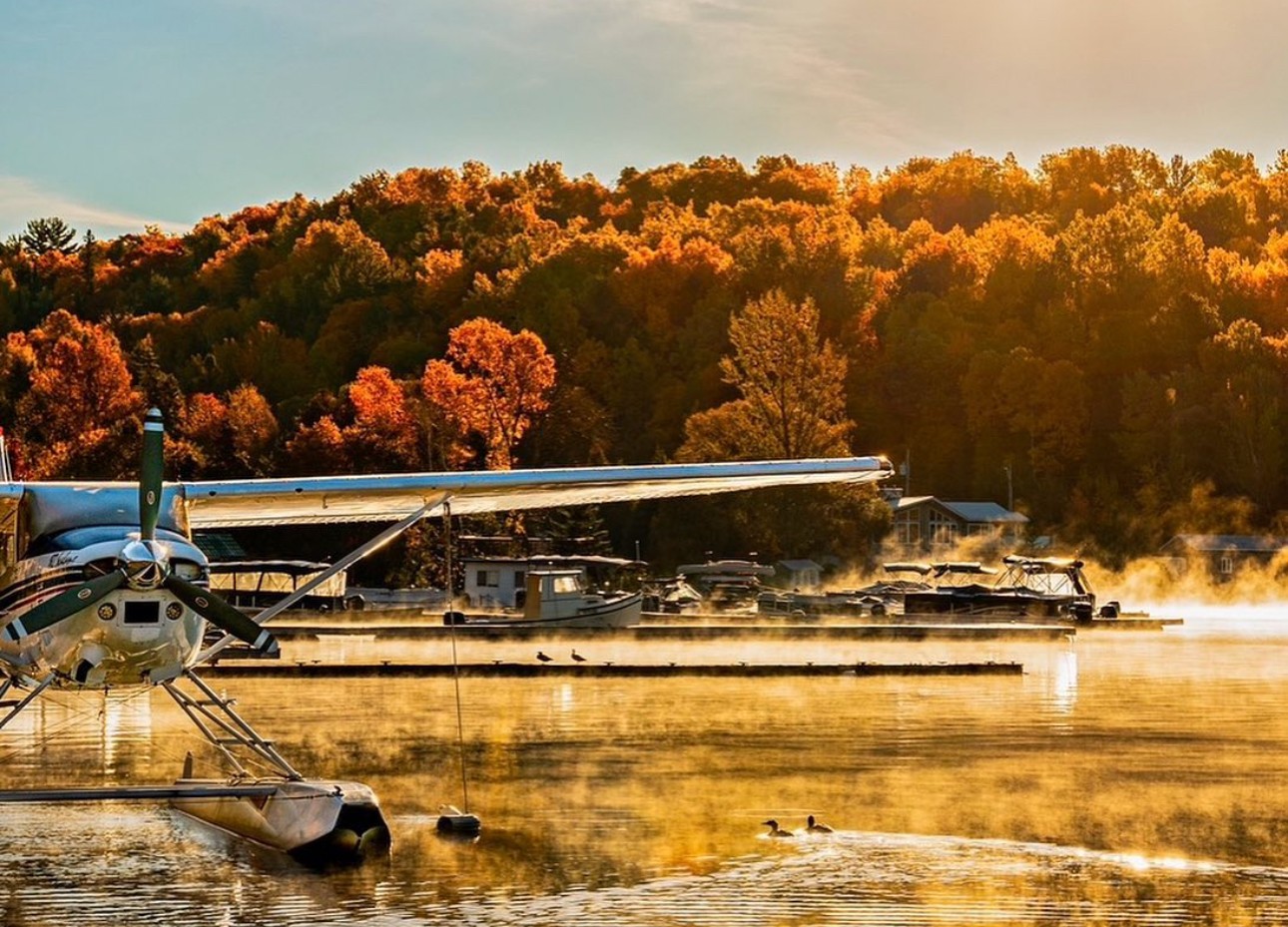 A float plane sparkles in the sunshine against a backdrop of orange trees on Trout Lake in North Bay