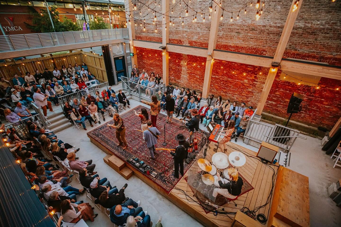 A band plays on a central outdoors stage at the Refetorrio in Sudbury while audience members happily listen on the cement steps that surround it. 
