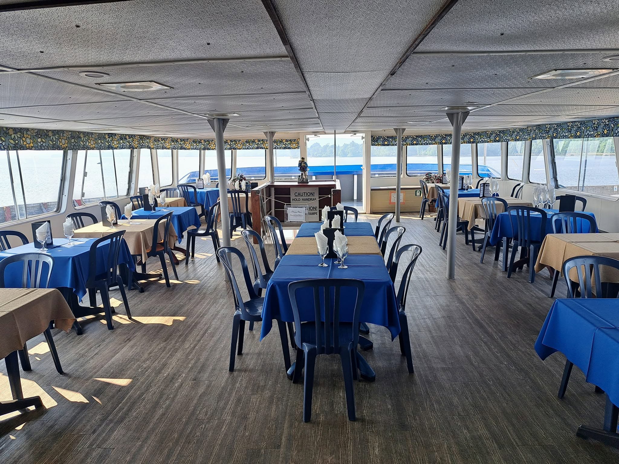 the lower deck of the Chief Commanda 2, set with rows of tables laid for dinner with matching blue tablecloths, surrounded by bright windows in all directions.