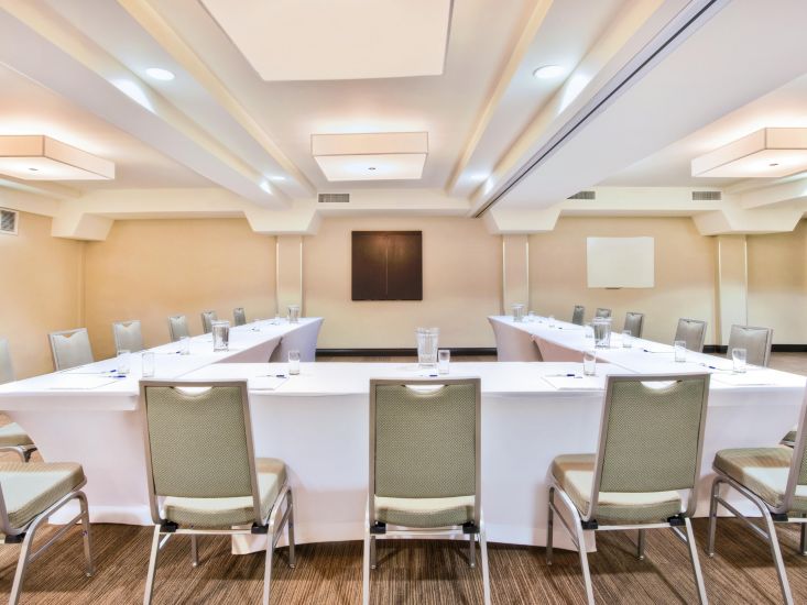 long tables with white table cloths set up in a square under modern white light fixtures in a in a clean, modern boardroom set up at the Holiday Inn Express Sault Ste. Marie. 