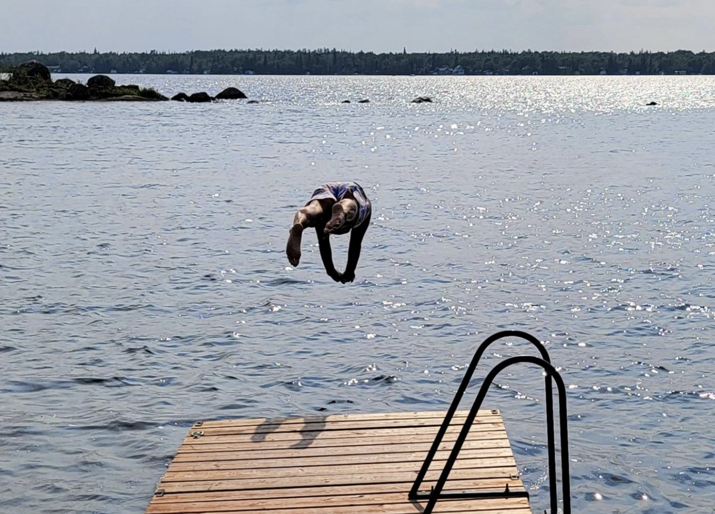 a person dives off a wooden dock into a blue lake on a clear summer day.