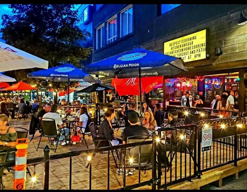 a full patio on a summer night, lit up in the evening light under a sign that says "Respect is Burning Kitchen and Bar".