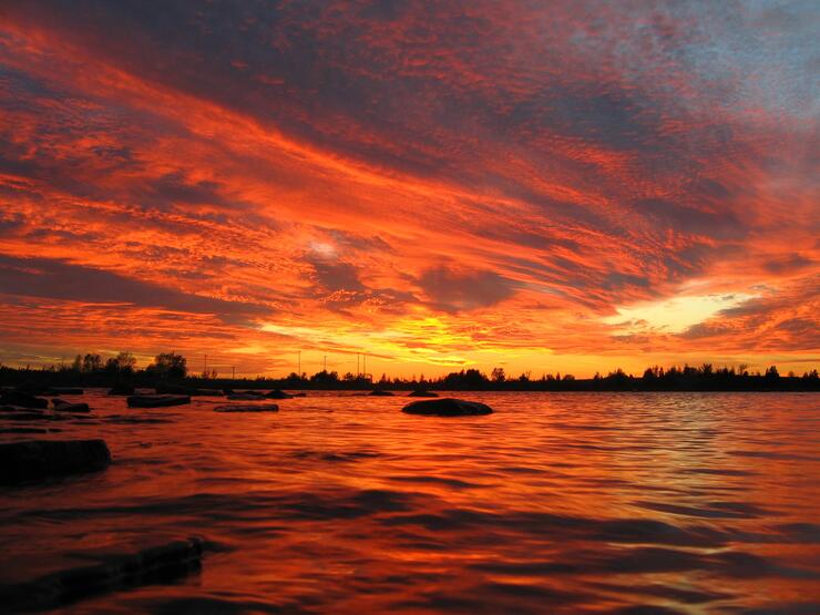 The Manitou Islands in Lake Nipissing silhouetted black against a vivid orange sunset with swirling clouds above.