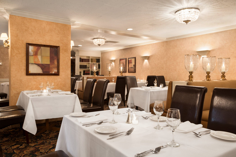Tables in a dining room decorated with white linen and china under soft lamplight at the Senator Hotel. 