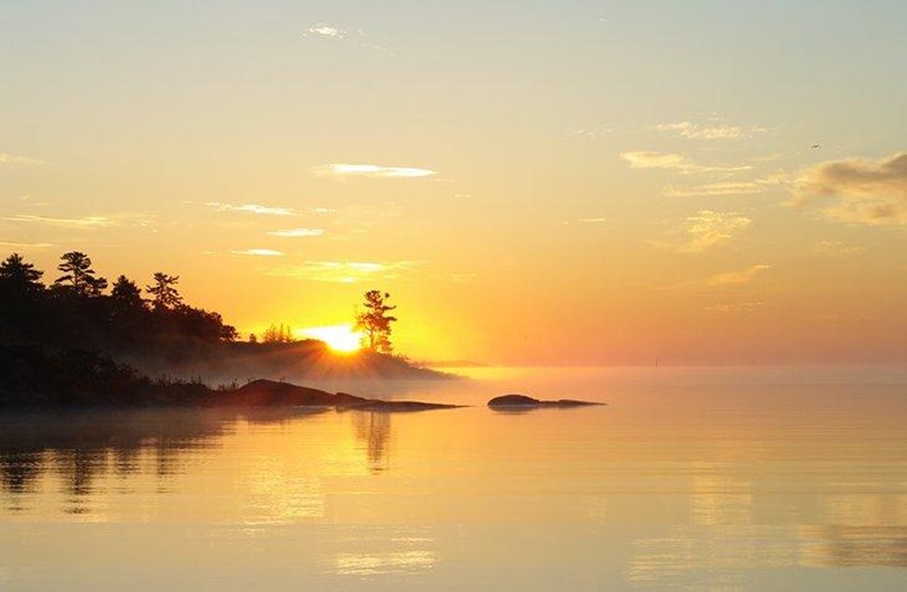 a bright golden sunrise shines through the mist over a glassy lake in Northern Ontario. 