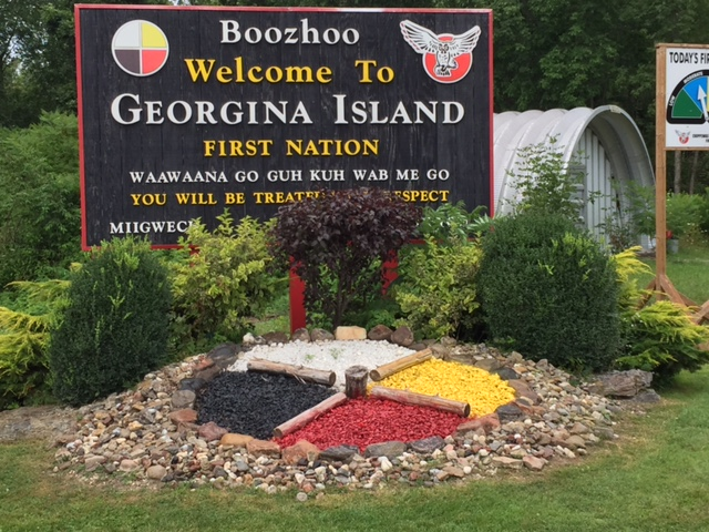 A sign with a rock medicine wheel at the base that reads "Welcome to Georgina Island First Nation".