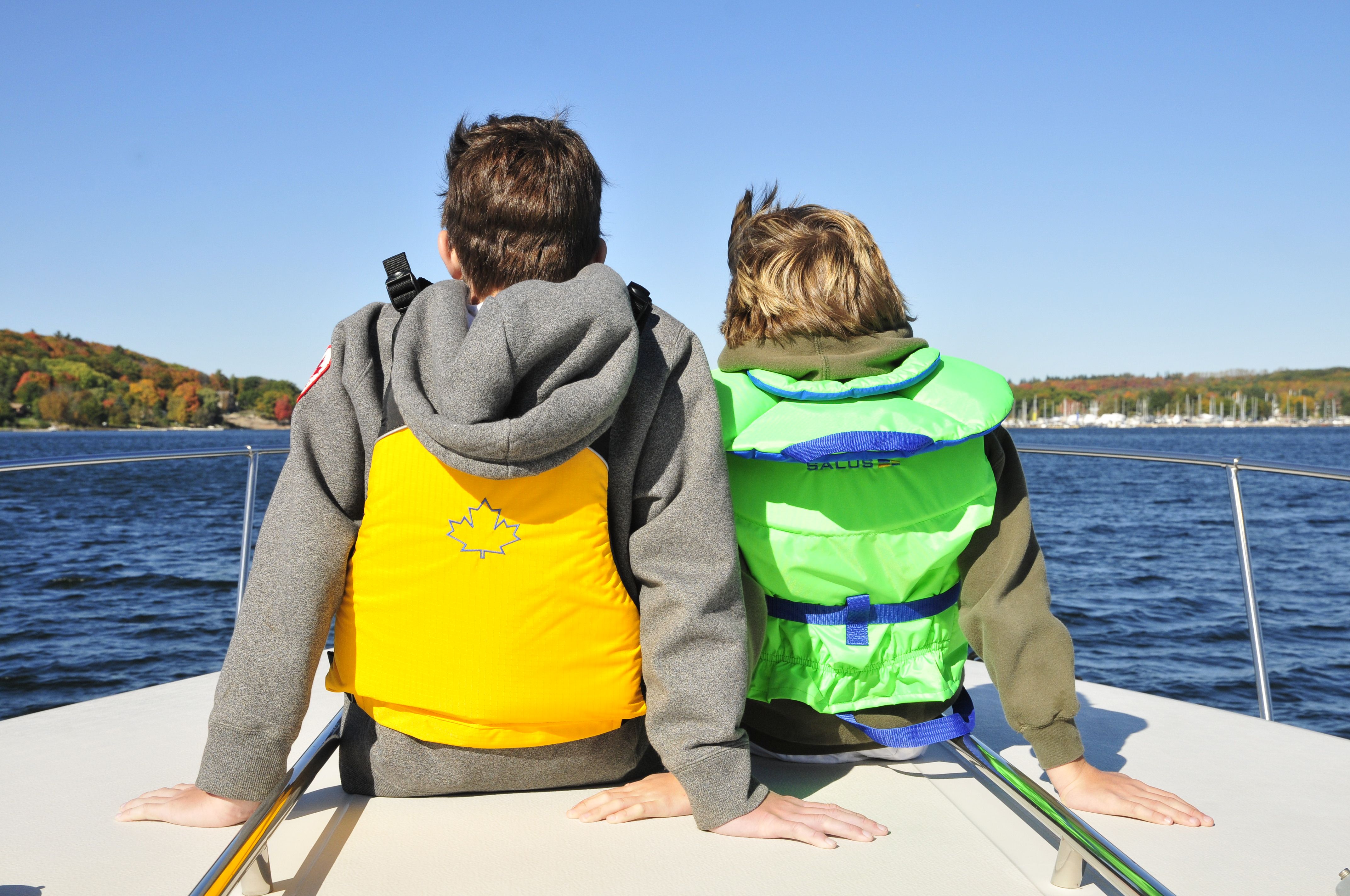 two people sit wearing life jackets on the bow of a boat, looking out over the breezy lake on a clear blue day. 