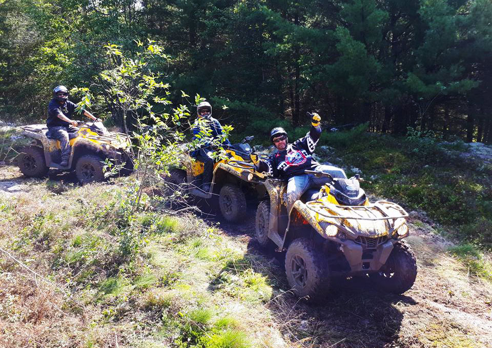 Three ATVers pose and joke on their ATVs on a forest trail. 