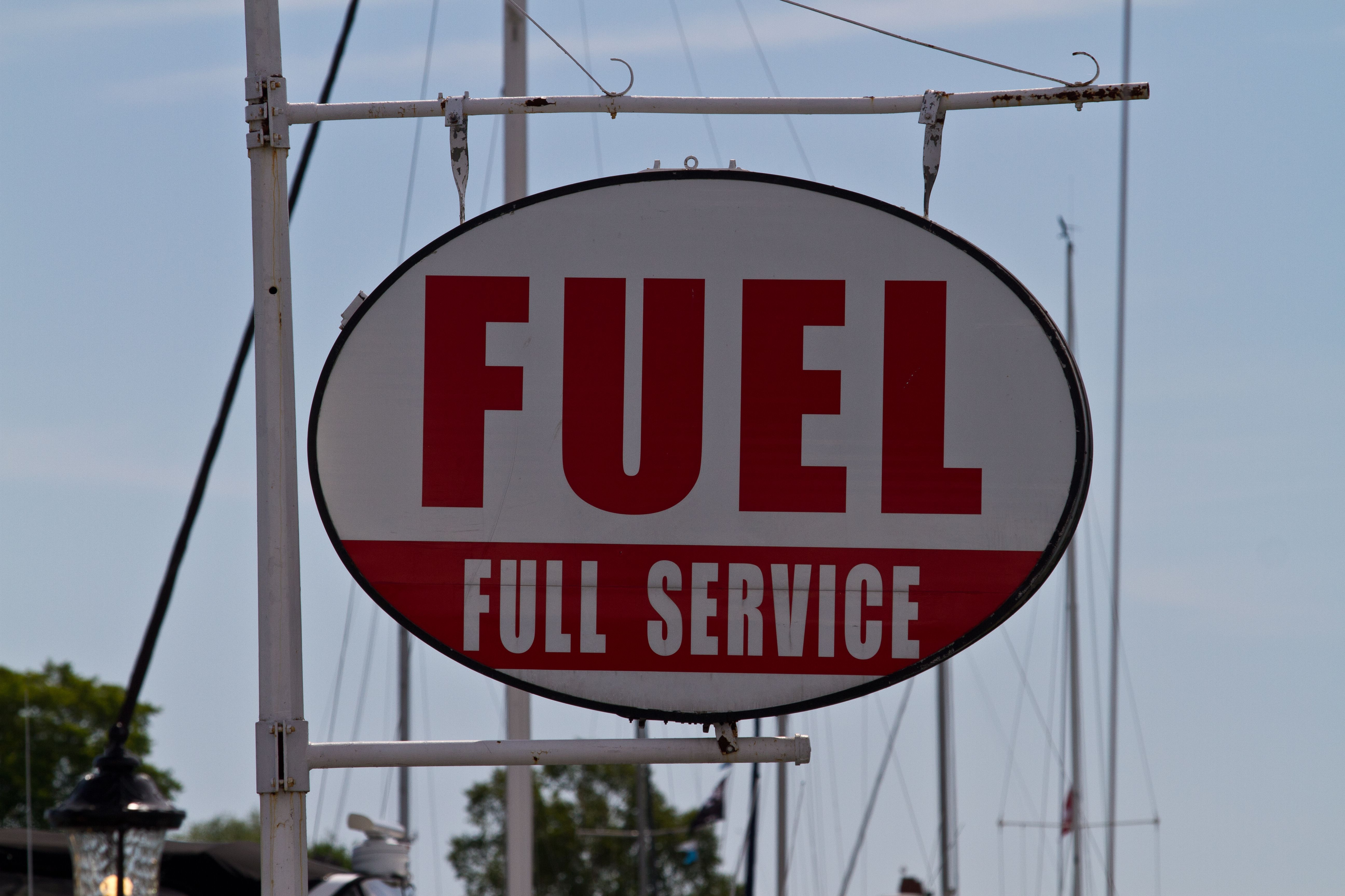 an oval marina sign that reads "Fuel Full Service" hangs overhead in front of a clear blue sky.