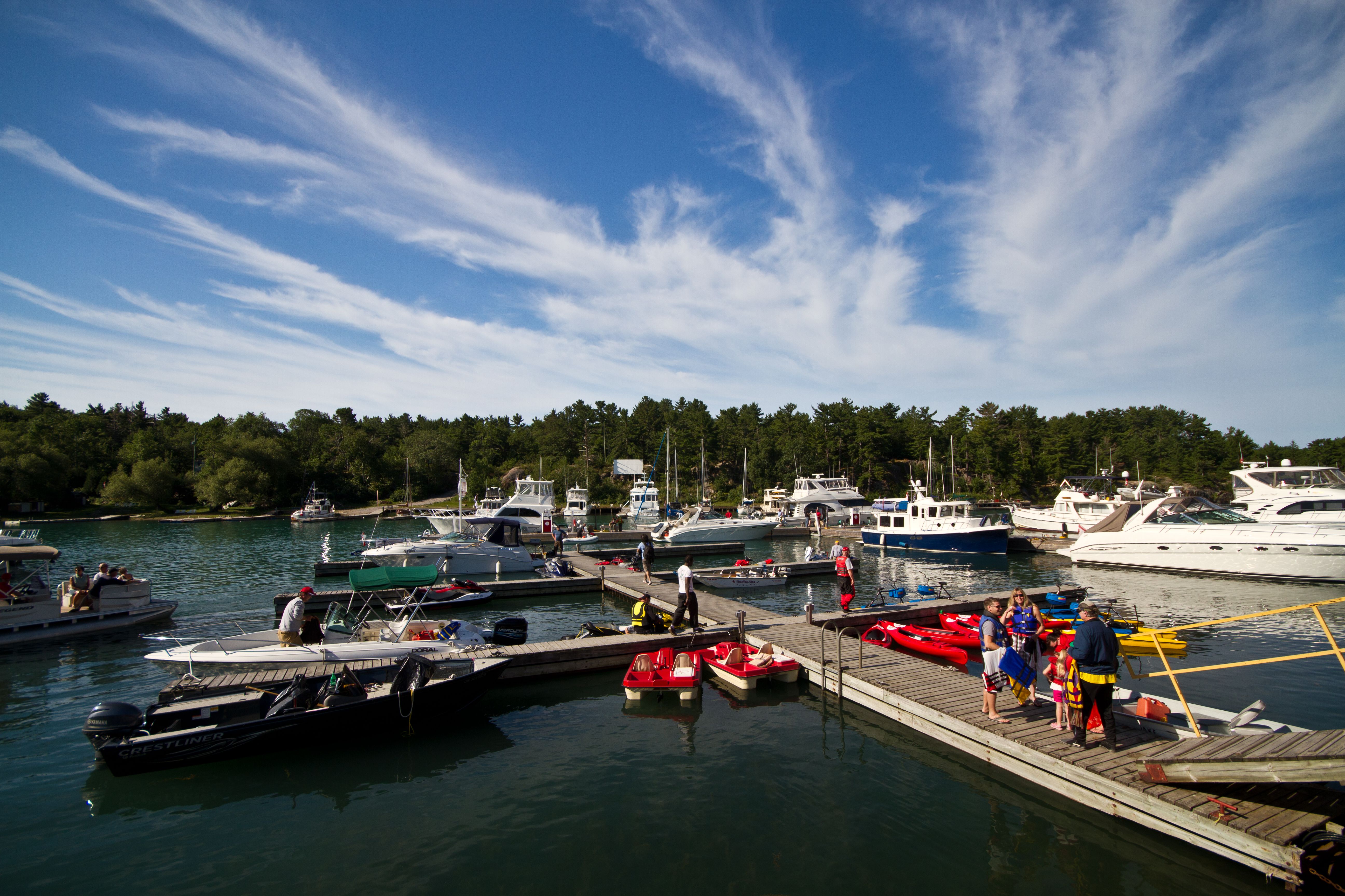 a people chatting and readying their boats on the docks at Killarney Marina under a vivid blue summer sky. A family dons life jackets as their guide hands them out. 