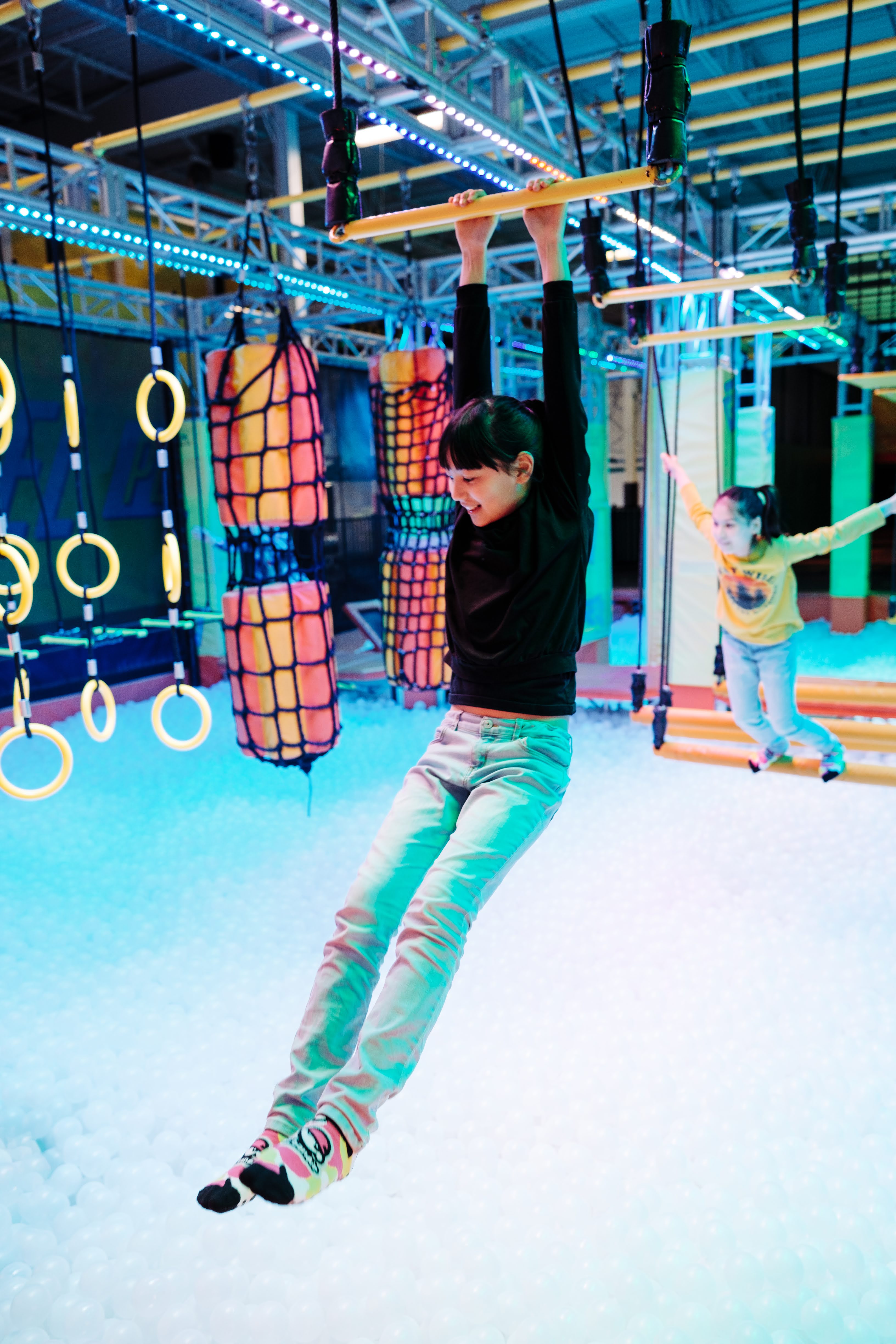 a smiling child hangs from some climbing bars in a glowing, blacklit climbing course at Urban Air.