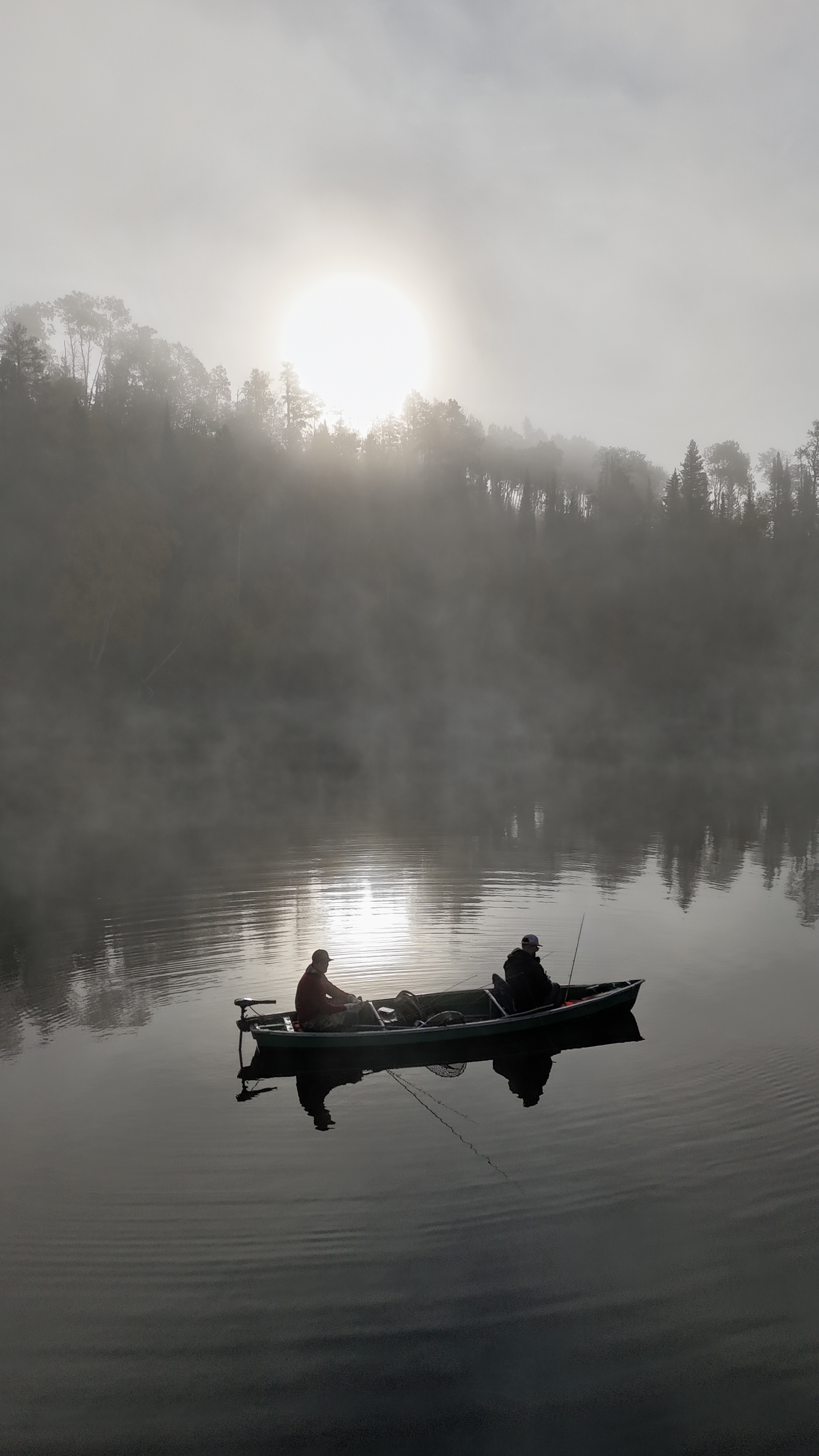 sunrise on the water shines on two men in a canoe, fishing