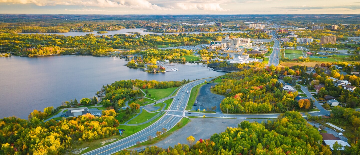 The city of Sudbury stretches out around the edge of Lake Ramsey, with highways and buildings interspersed among green and yellow autumn forest stretching off into the distance.