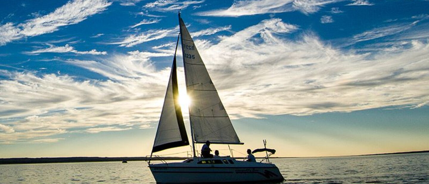 A sailboat floats along on calm waters reflecting a beautiful, vivid gold and blue sunset. 