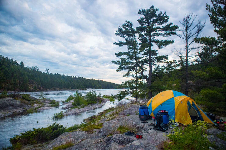 Tent set up on a smooth rock shoreline along a river.