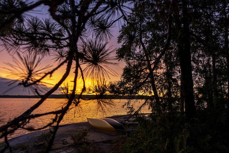Sunset over a lake, inverted canoes along the shore.