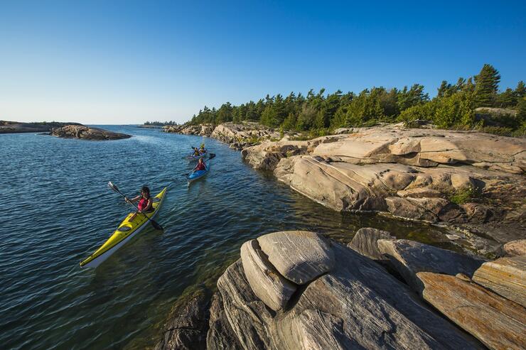 Kayakers paddling in turquoise water beside rocky island.