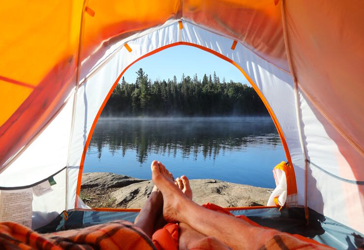 Two people's legs and bare feet looking out of a tent at a lake. 