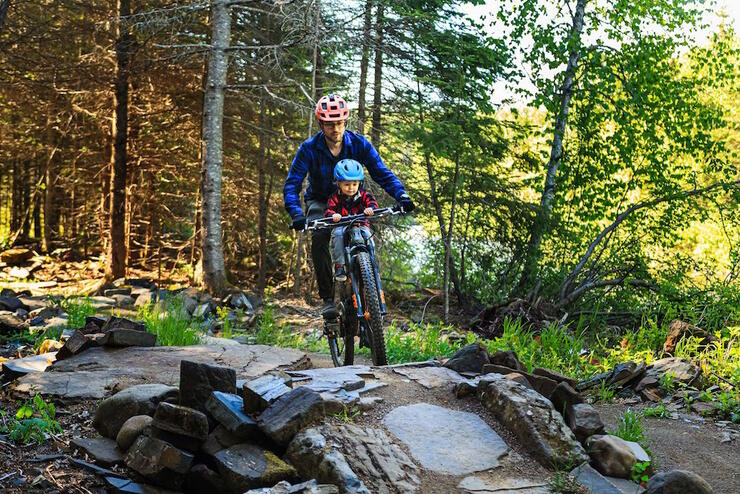 Man with young son on mountain bike riding on rocky trail in forest