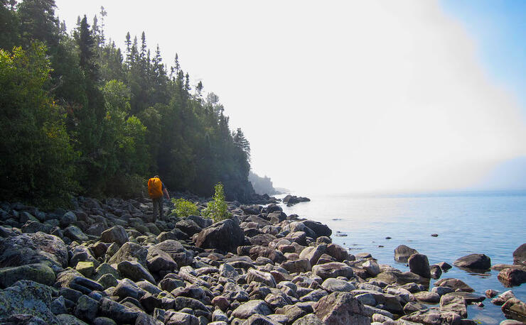Man with backpack hiking on large boulders on shore of Lake Superior