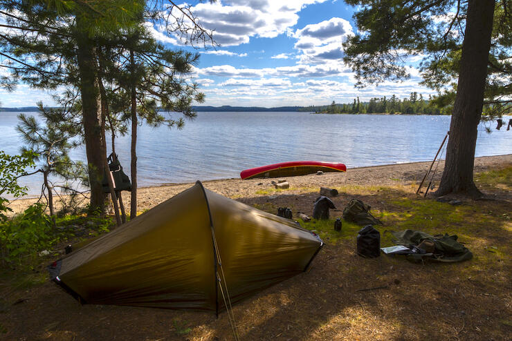 Crown land camping in Ontario with a small tent set up on the edge of forest with a canoe beside a lake.