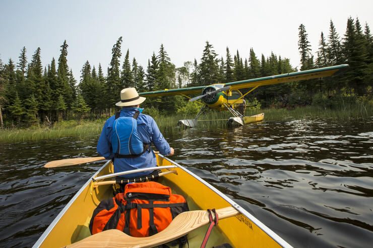 Man in bow of a canoe looking at a float plane. 