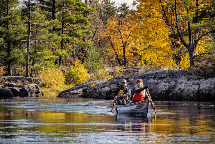 Two people paddling a canoe on a river with rocky outcrops. 