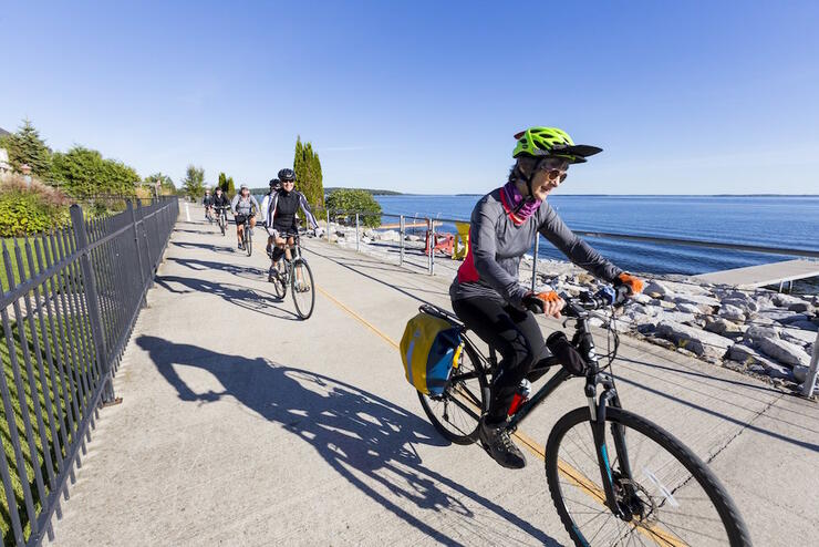 Group of cyclists riding along a paved path along a waterfront. 